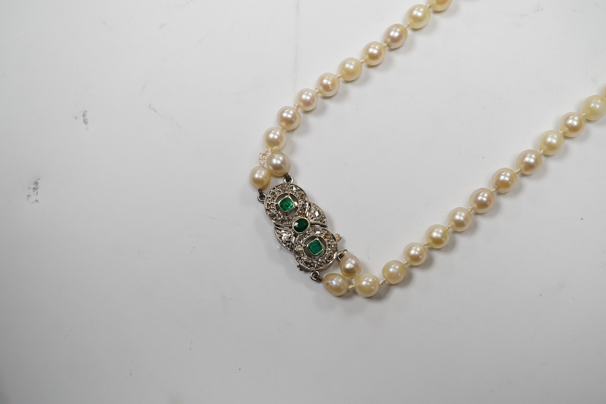 A single strand cultured pearl necklace, with and emerald and diamond cluster set white metal clasp, 76cm. Condition - fair.